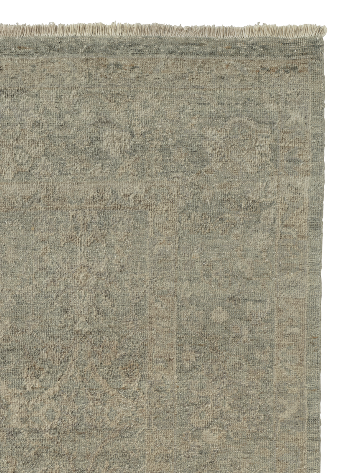 A close-up of a textured area rug with a distressed, vintage pattern in muted grey-green, beige, and taupe tones, featuring a fringed edge at the top | Armadillo Adagio Rug